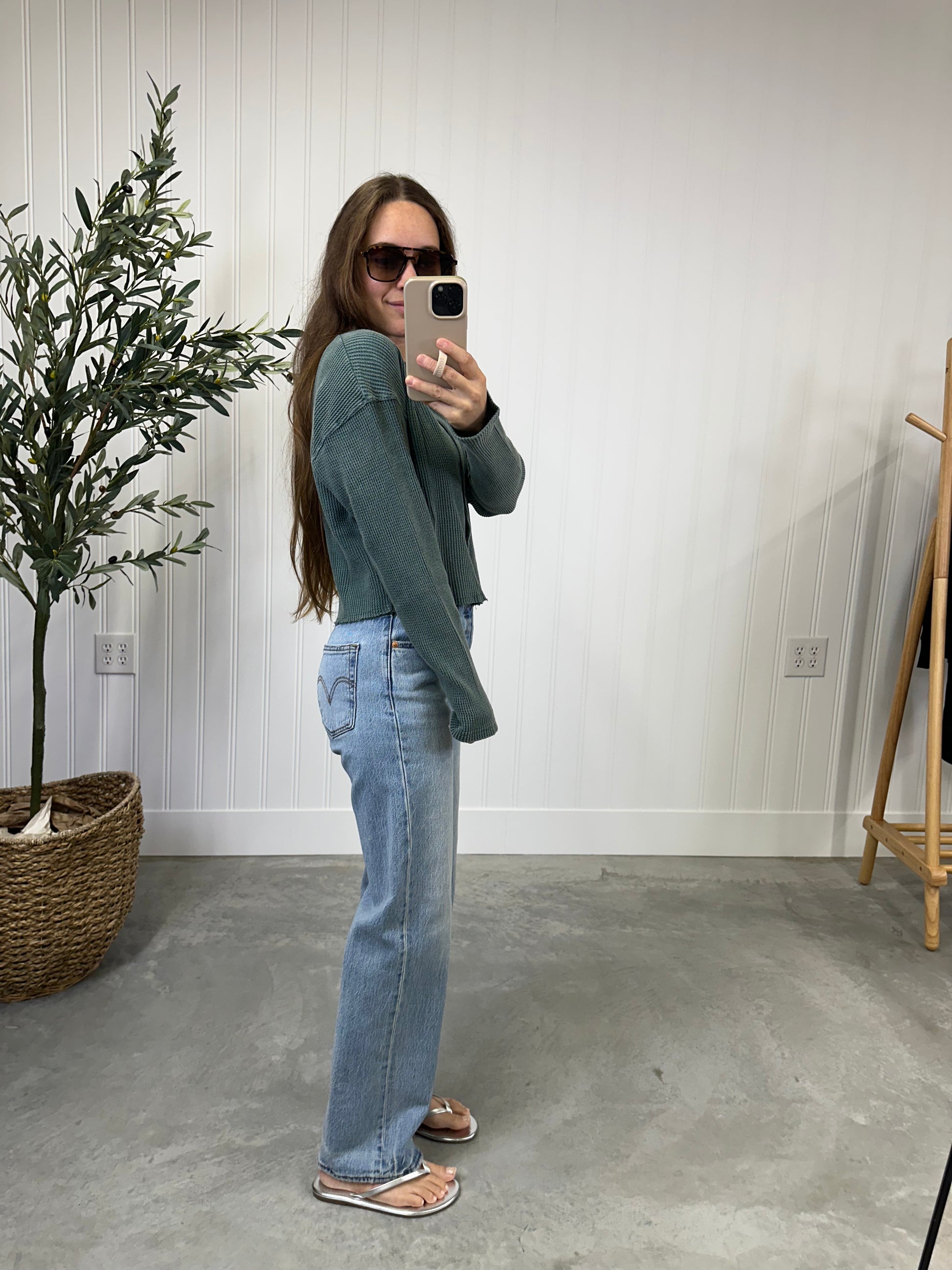 Person taking a mirror selfie wearing a green sweater and blue jeans in a room with a plant and coat rack. Evergreen Waffle Top