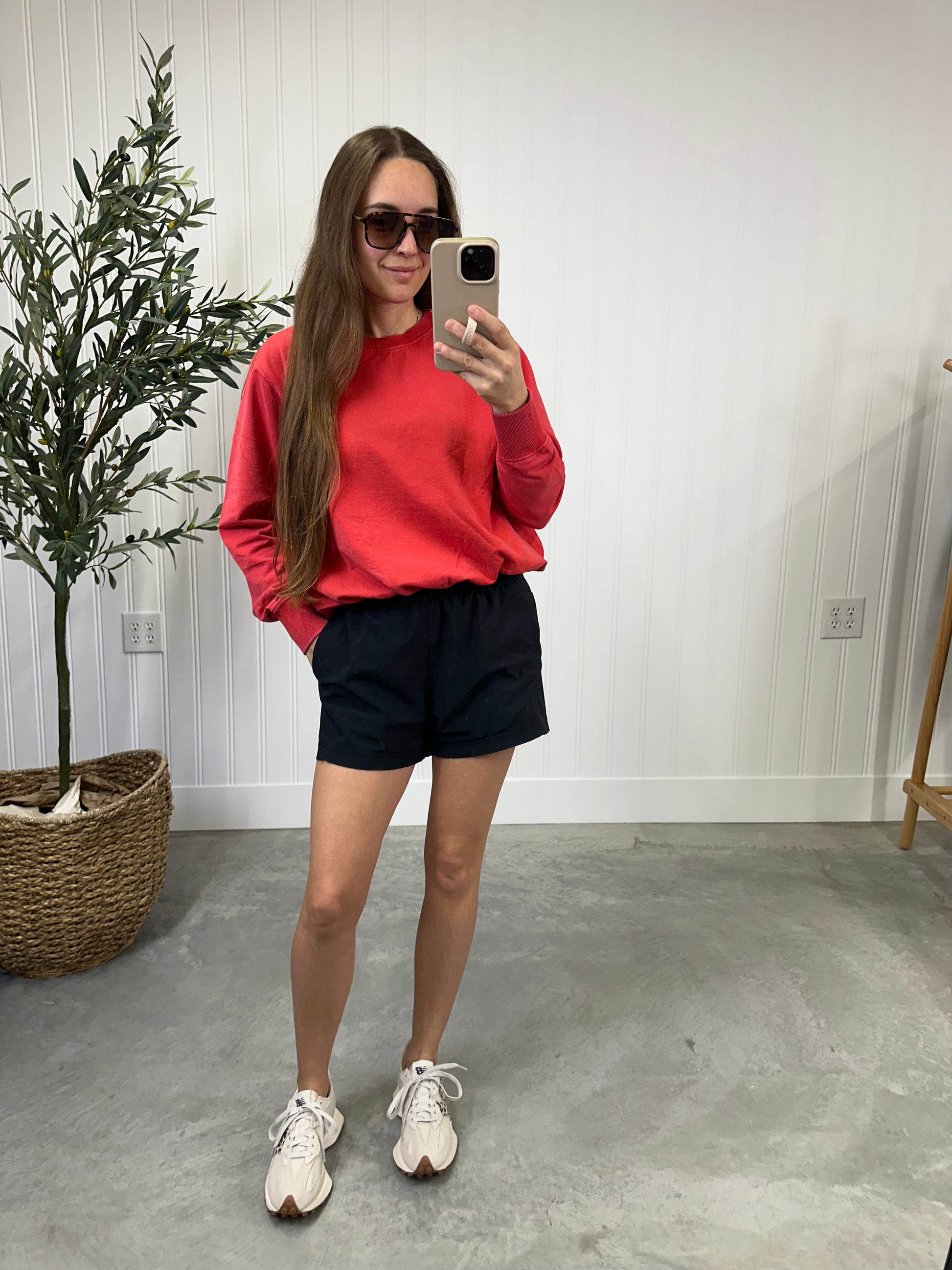 Person wearing a red sweatshirt, black shorts, and white sneakers taking a mirror selfie. Glazed Cherry Bubble Pullover