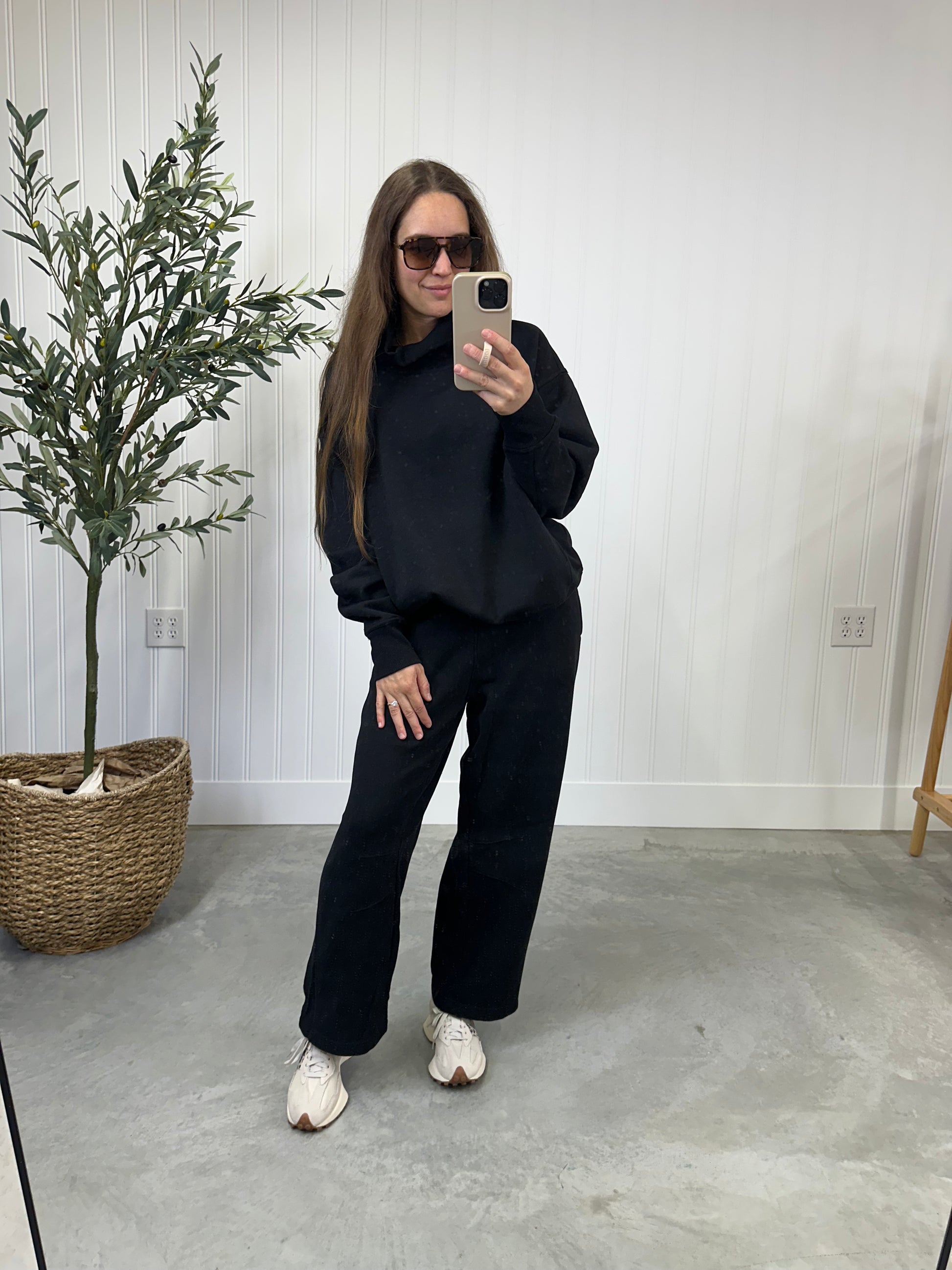 Person wearing a black outfit taking a mirror selfie in a minimalistic room. The Onyx matching lounge set.